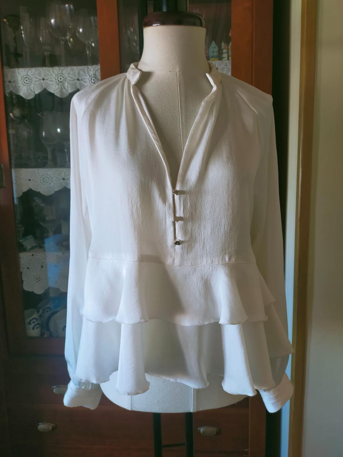 White chiffon blouse with ruffles on a mannequin, wardrobe background with crystal glasses and decorative details.