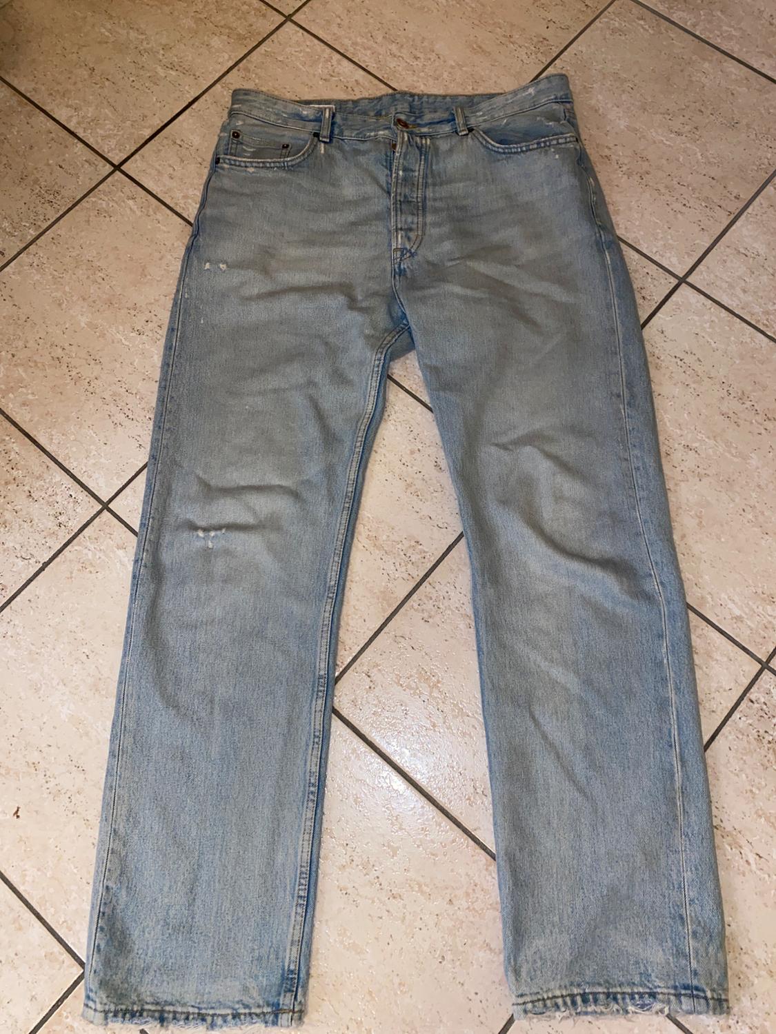 Front view of light blue jeans with front pockets and button fastening.