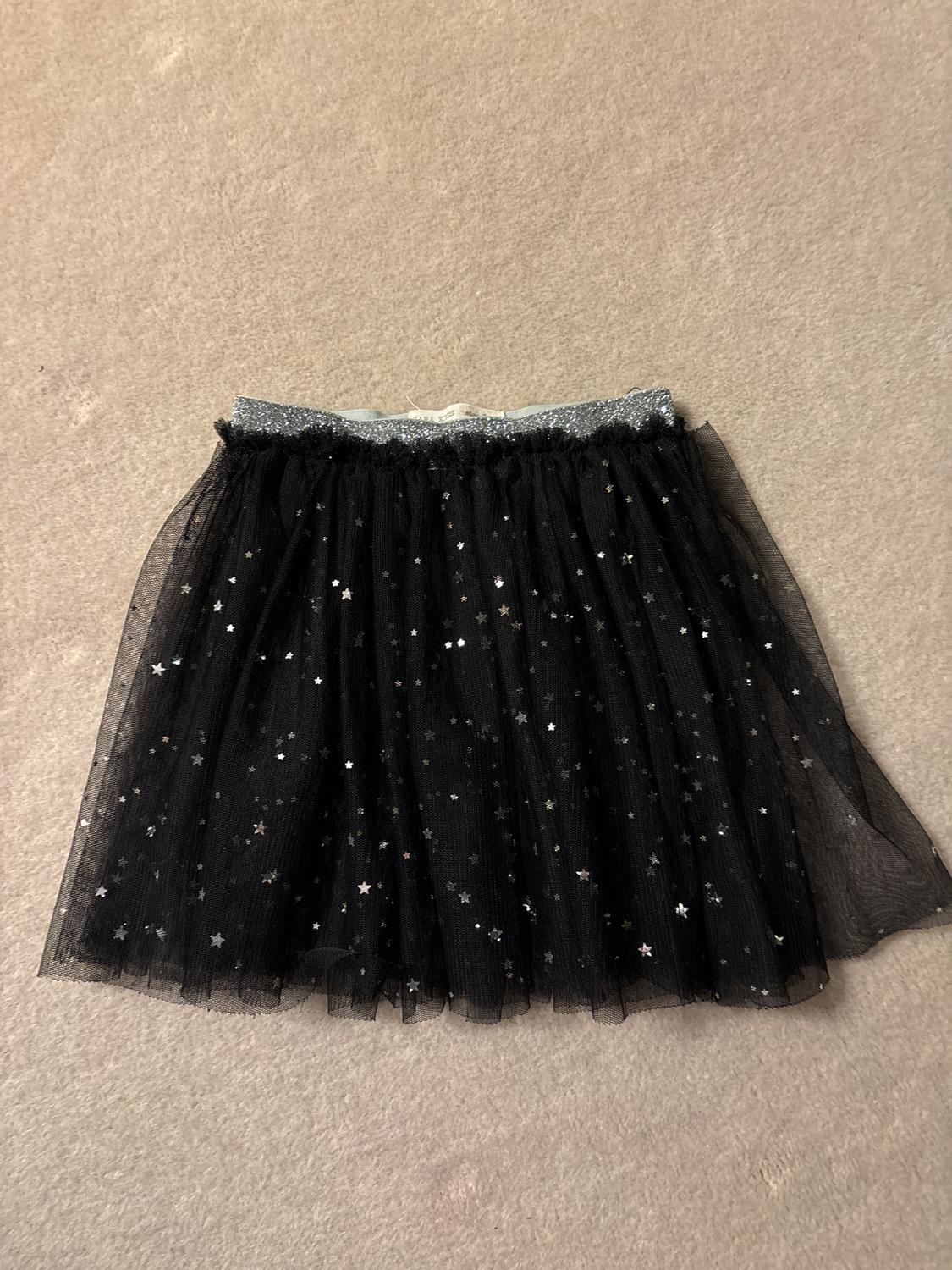 Black tulle skirt with a sparkly waist and silver star print on a beige background.