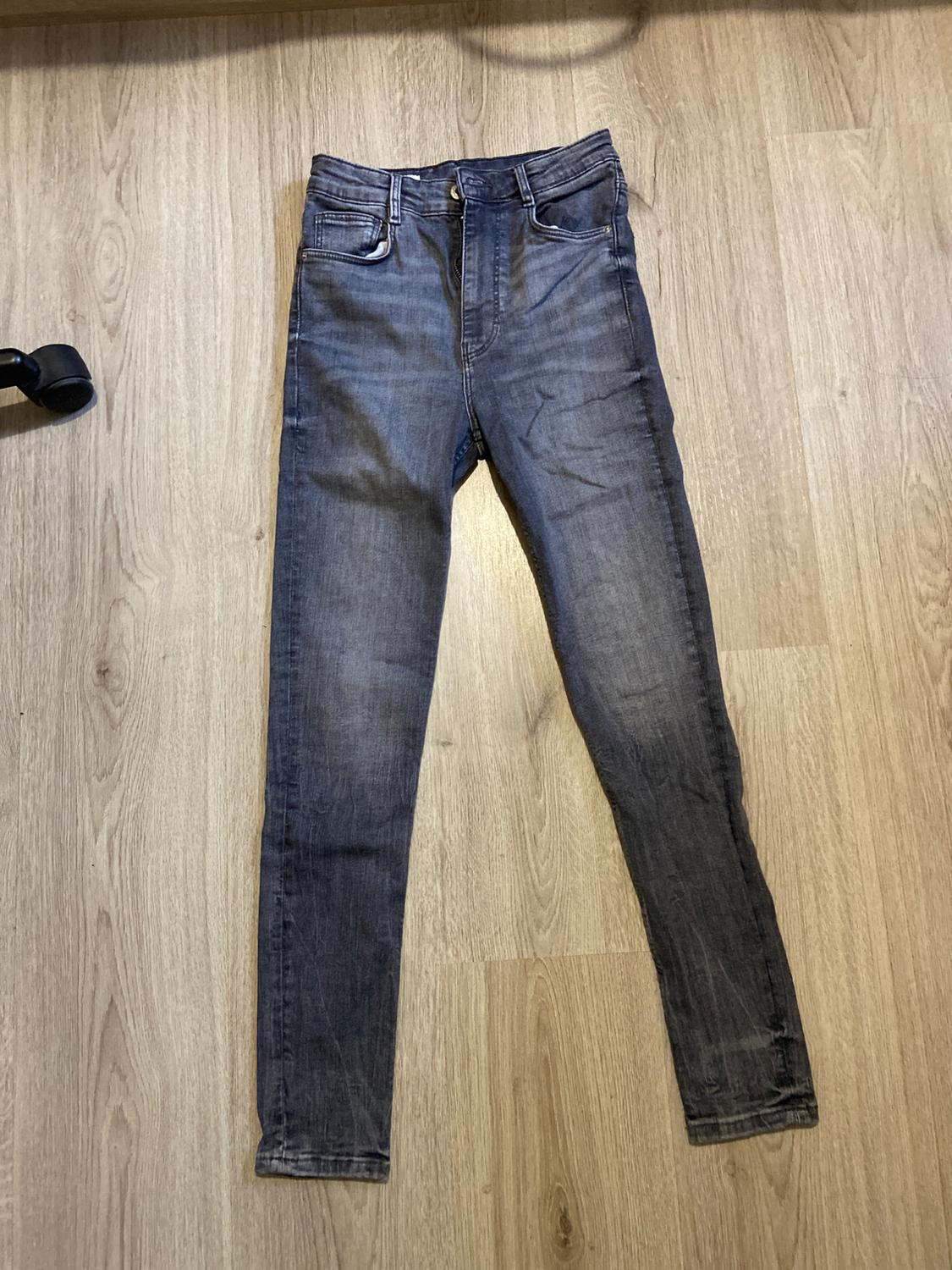 Dark blue denim skinny jeans with a distressed effect, laid on a light wood floor.