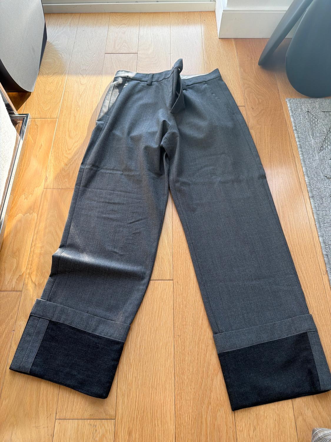 Gray wide-leg pants with a dark hem, placed on a light wooden floor, illuminated by natural light.