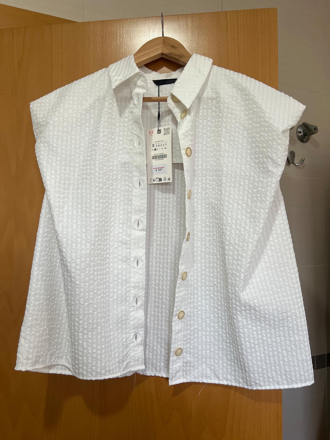 White shirt with a checked texture, hanging on a wooden hanger. Visible label with price and size S details.
