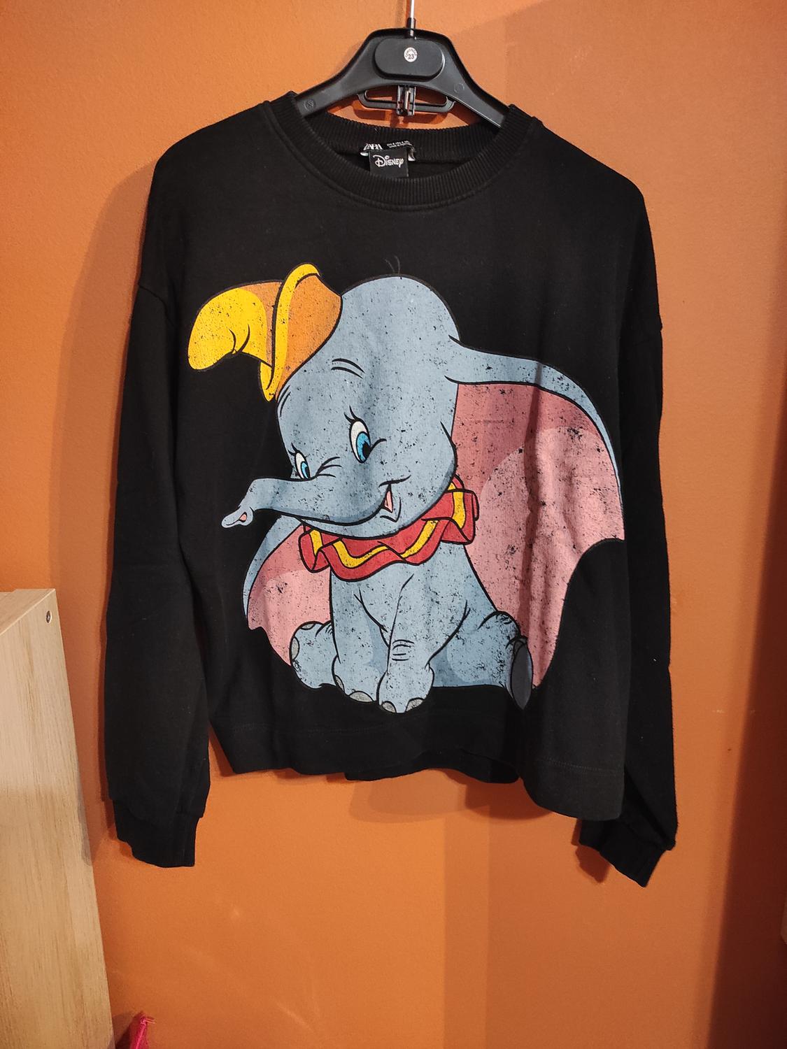 Black hooded sweatshirt with Dumbo print on the front. Orange background. Visible tag: "Disney".