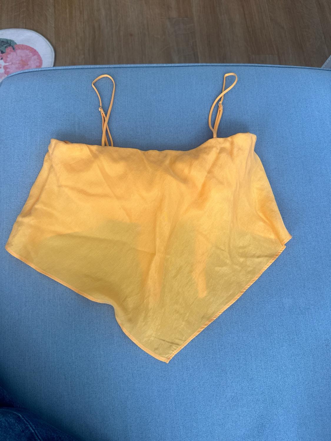 Lightweight yellow camisole top with a V-hem, on a light blue seat. Relaxed style composition.