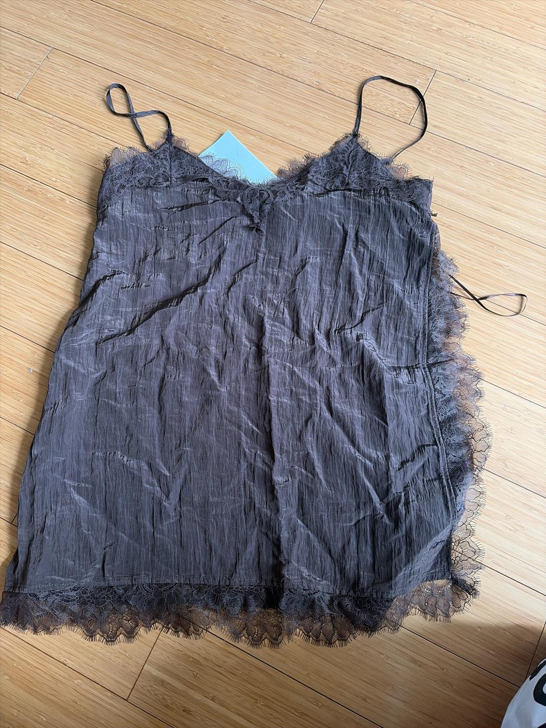 Dark gray wrinkled camisole top with thin straps and lace on the neckline, hem, and side, on a wooden floor.