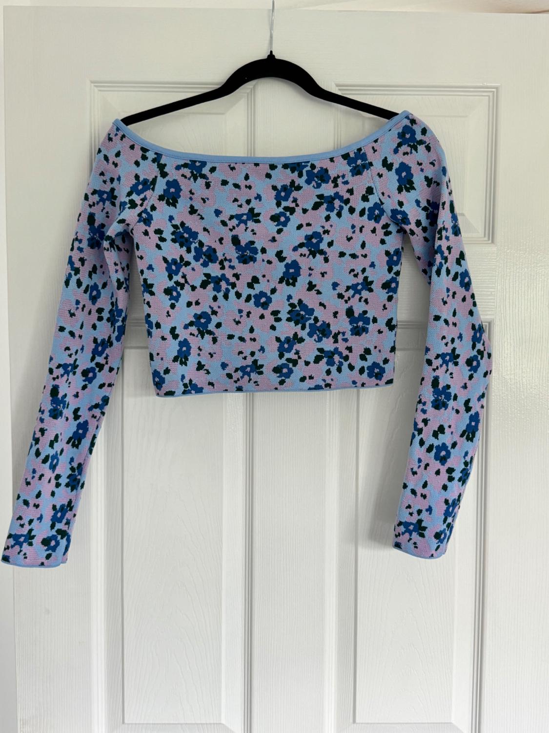 Long-sleeved top with a blue and black floral print on a lilac background, hanging on a black hanger in front of a white door.