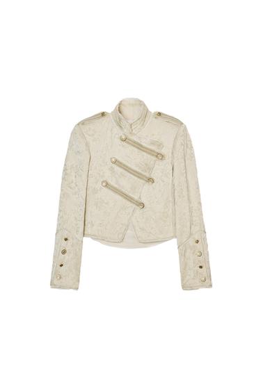 Front view of a short beige jacket with a funnel neck, long sleeves, embossed metallic buttons, and floral jacquard fabric.