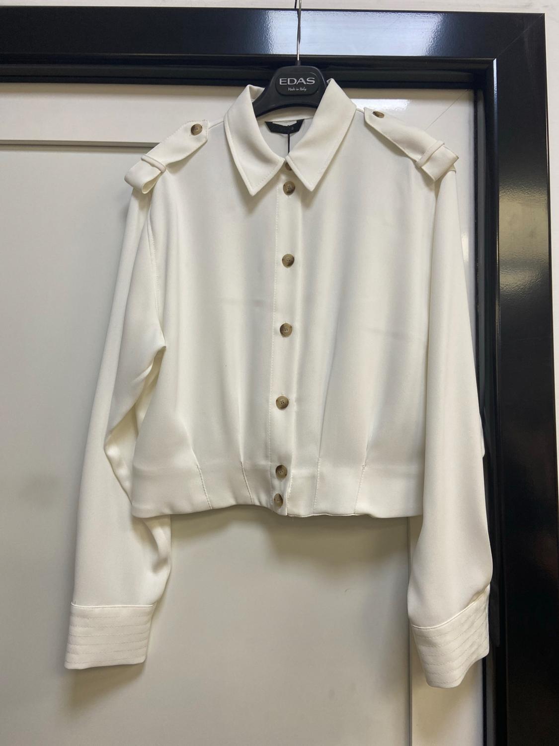 White long-sleeved shirt with buttons and epaulettes, on a black hanger bearing the text EDAS Made in Italy, in front of a white door.
