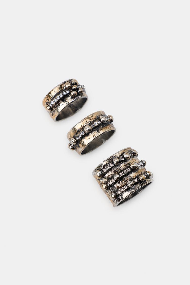 Balení tří prstenů v antracitově šedé barvě s prolamovaným designem a leskem, jeden široký a dva tenčí s reliéfními detaily.