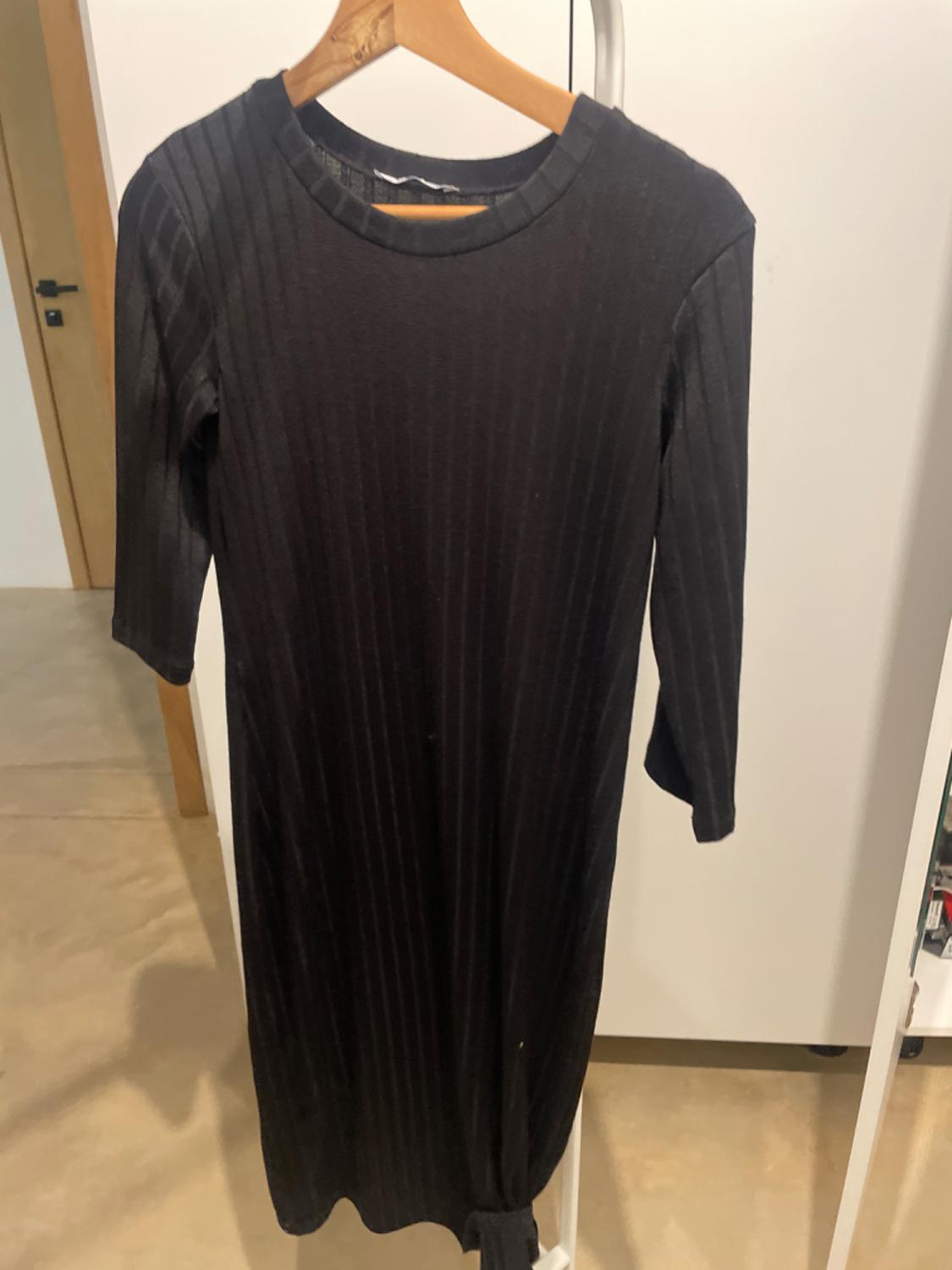 Long-sleeved black dress with vertical stripe texture, hanging on a wooden hanger in an indoor setting.