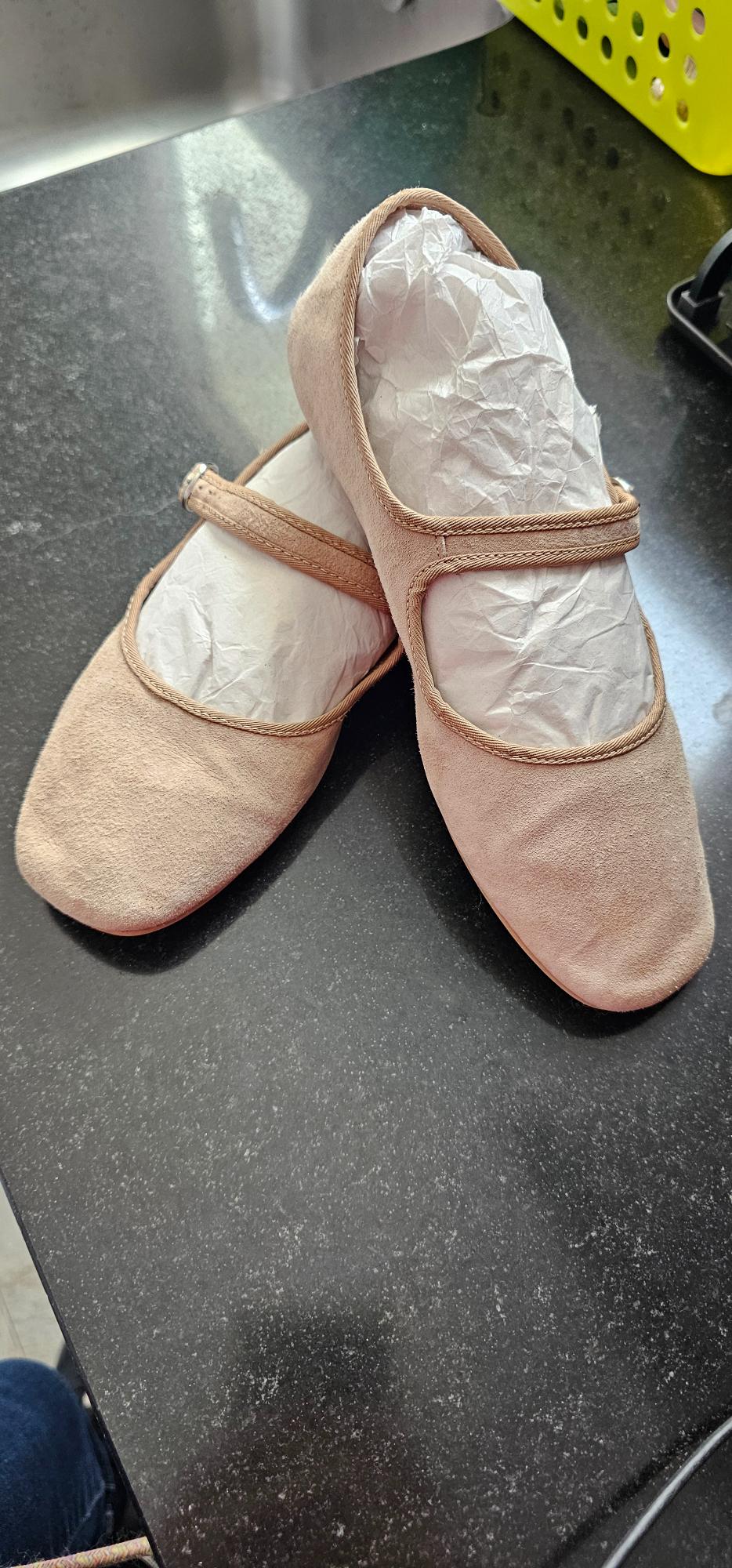 Beige flat shoes with a strap, stuffed with white paper, on a shiny black surface.