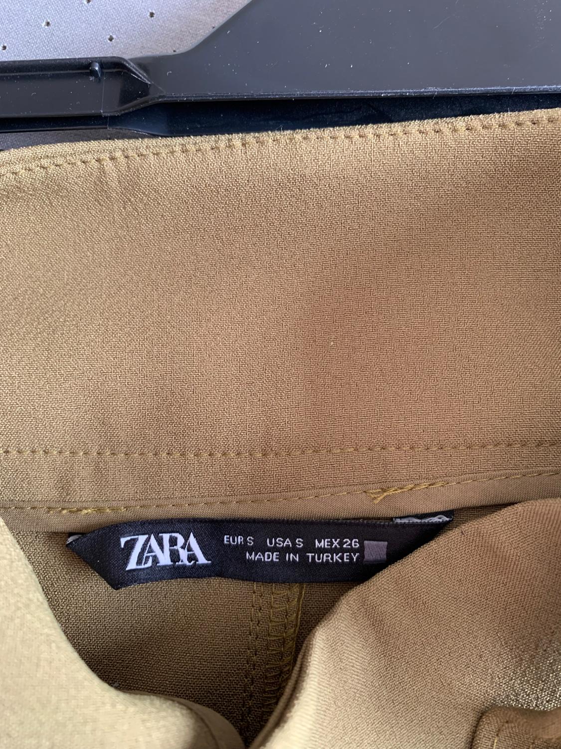 Beige garment tag with text "ZARA EUR S USA S MEX 26 MADE IN TURKEY" on a black hanger.