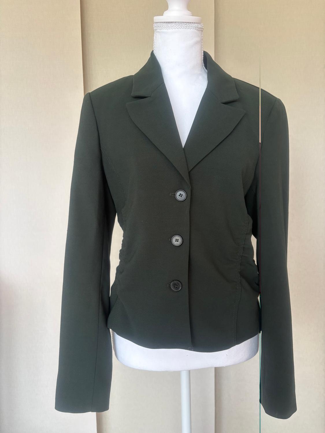 Dark green, three-button jacket on a white mannequin, beige background.