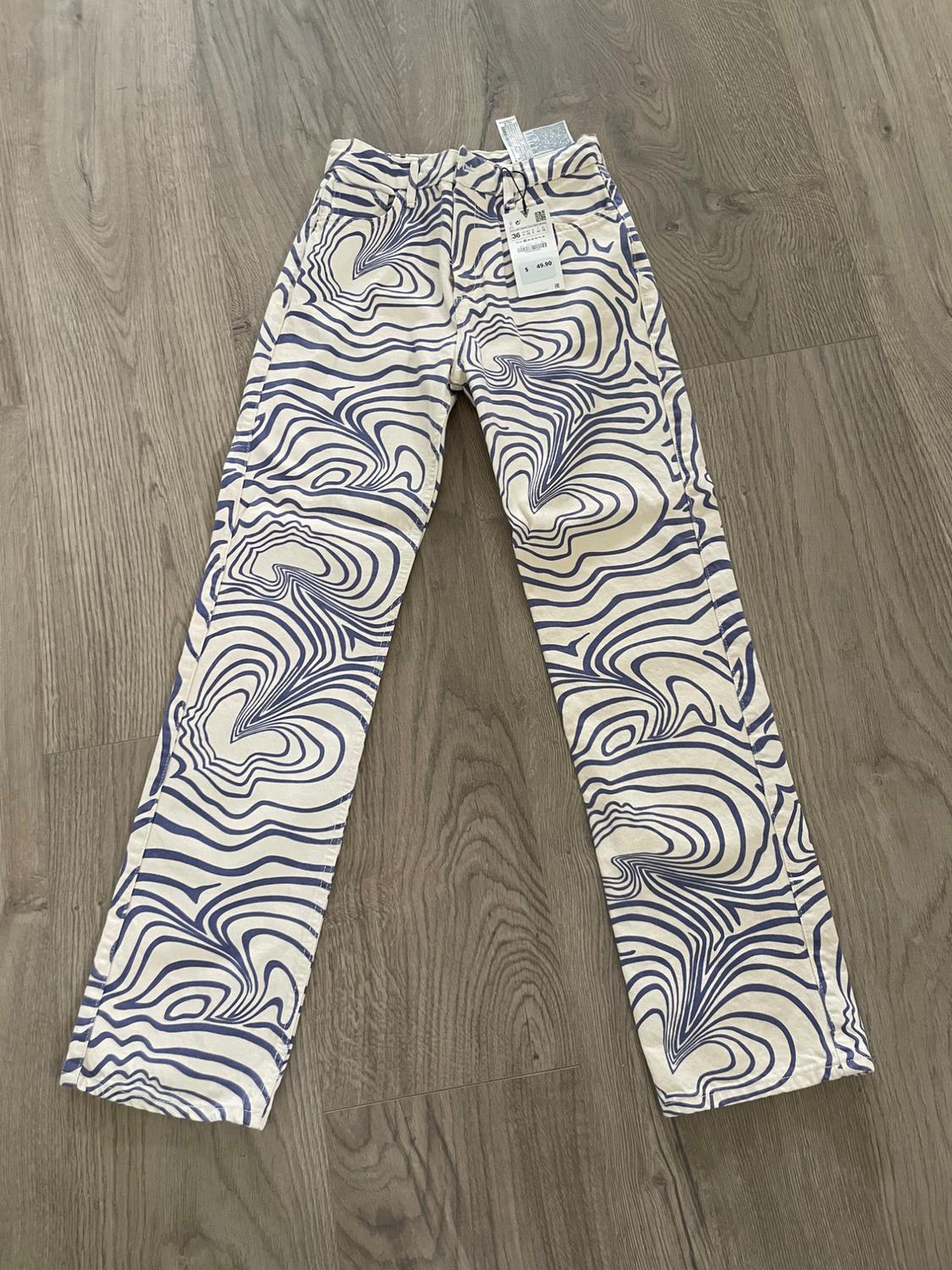 Pants with a dark blue wavy-line print on a light background, laid out on a wooden floor. Tag at the waist.