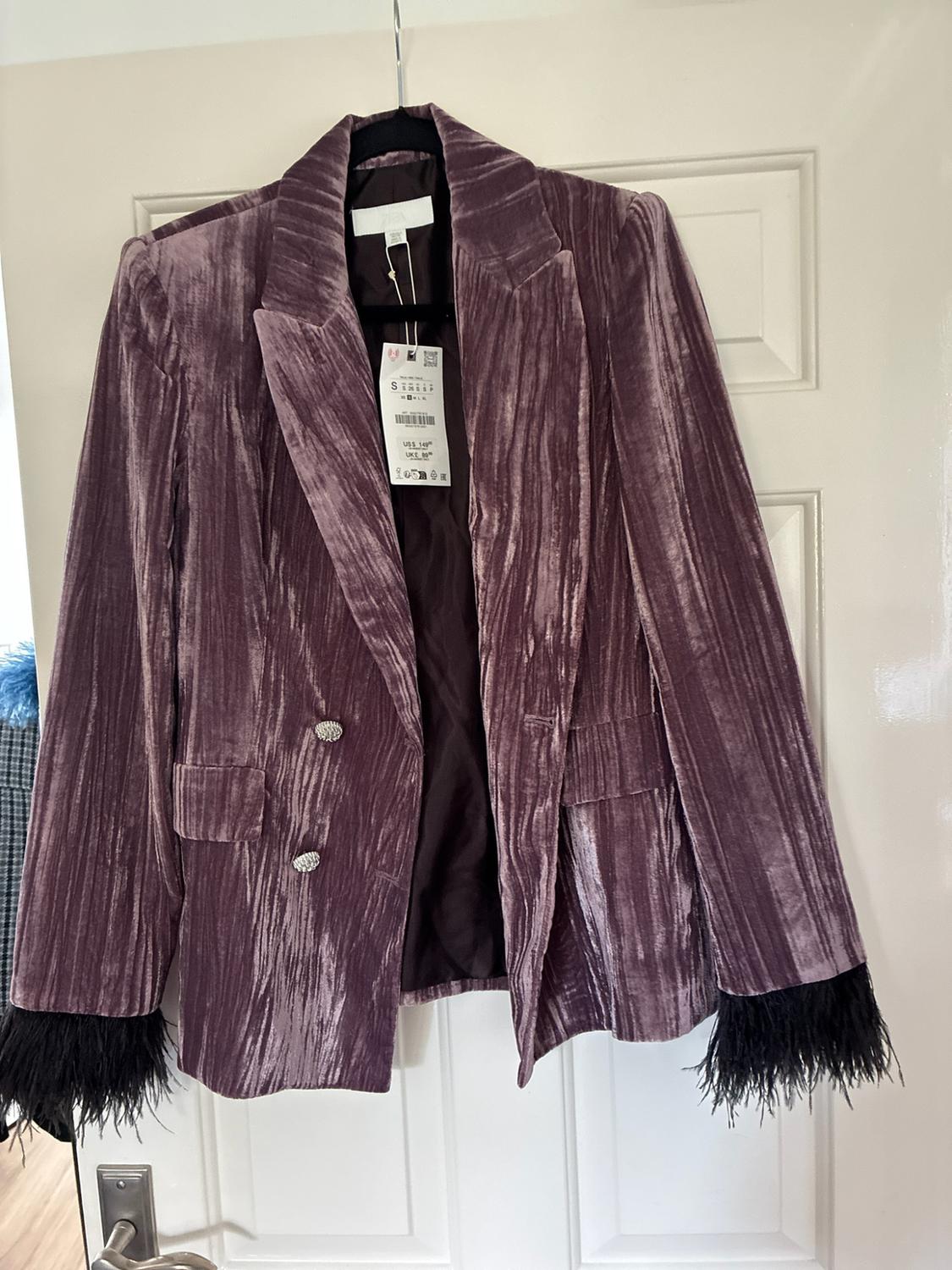 Crushed velvet purple blazer, silver buttons and black feathers on the cuffs, hanging on a white door. Text: S, US$ 149, UK£ 89.