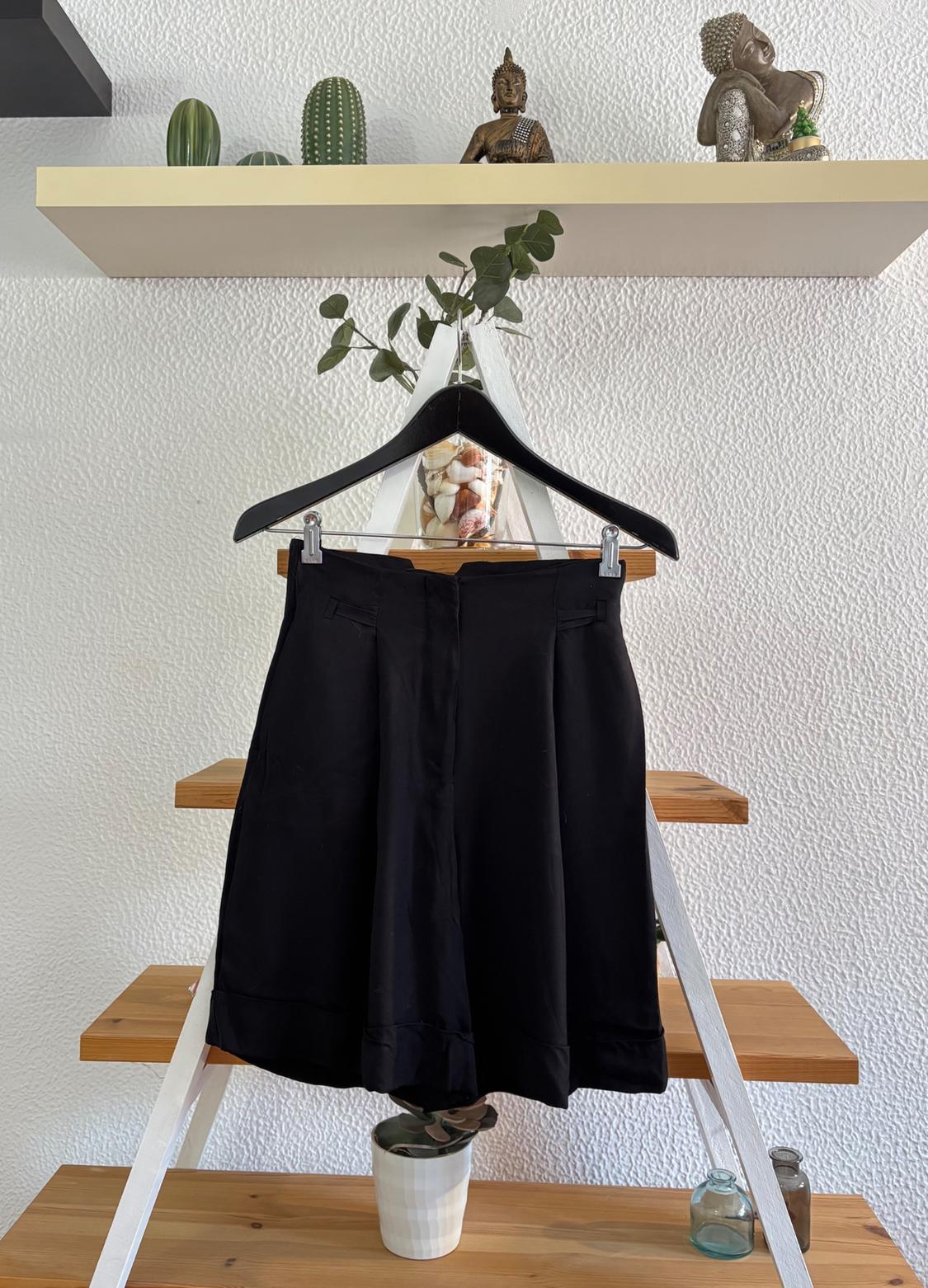 Black shorts hanging on a wooden ladder, with plants and figurines on a top shelf. White wall background.