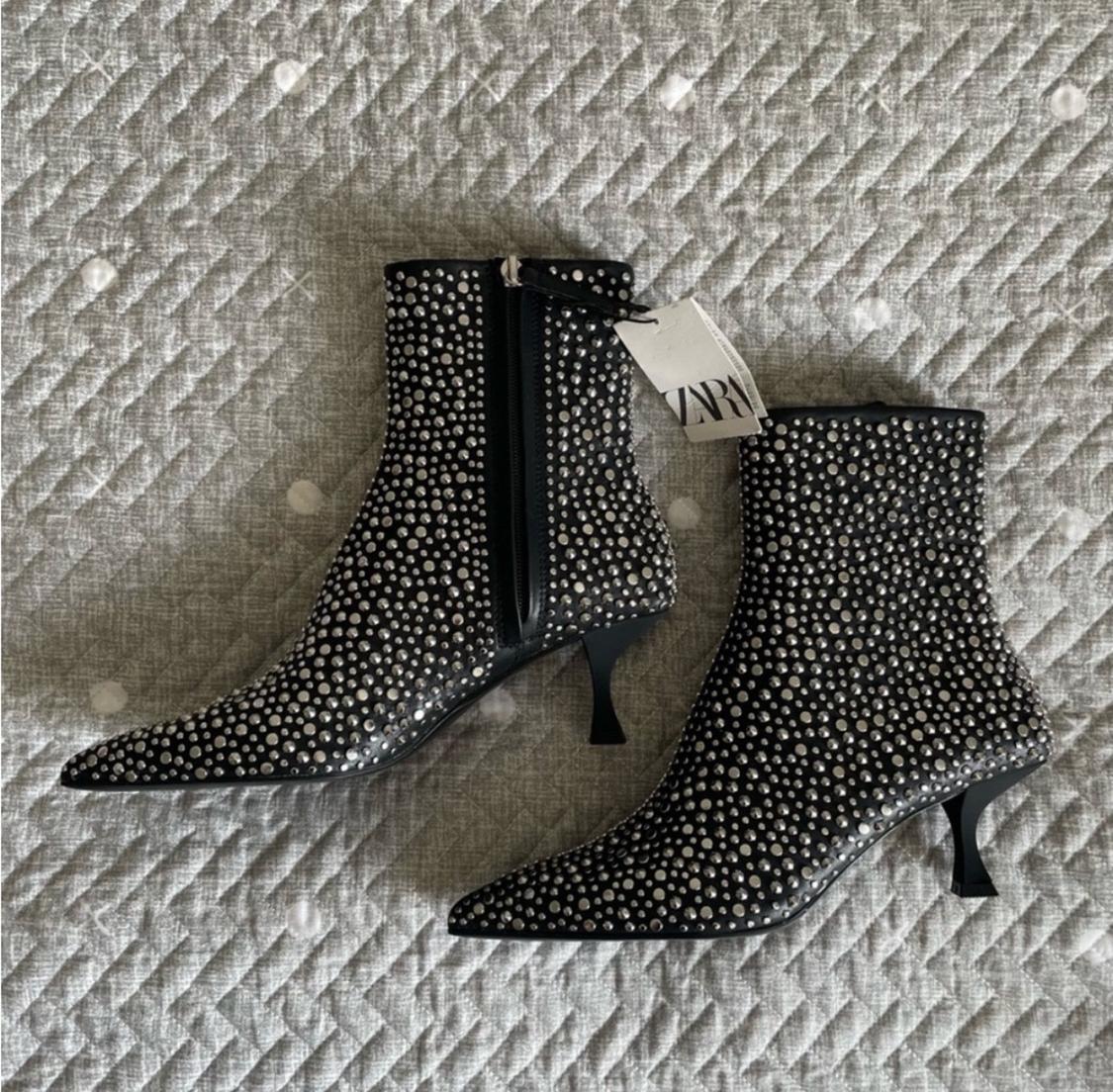 Black ankle boots with low heels and silver studs on a quilted gray bedspread. Visible label with text "ZARA".