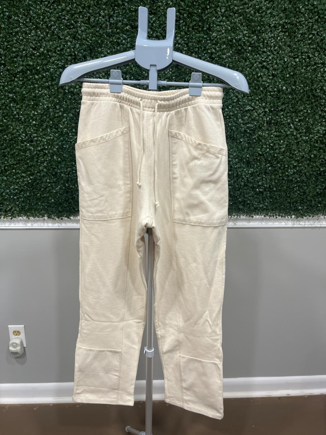 Beige pants hanging on a gray hanger, textured green wall background. Casual design with pockets and an adjustable drawstring.