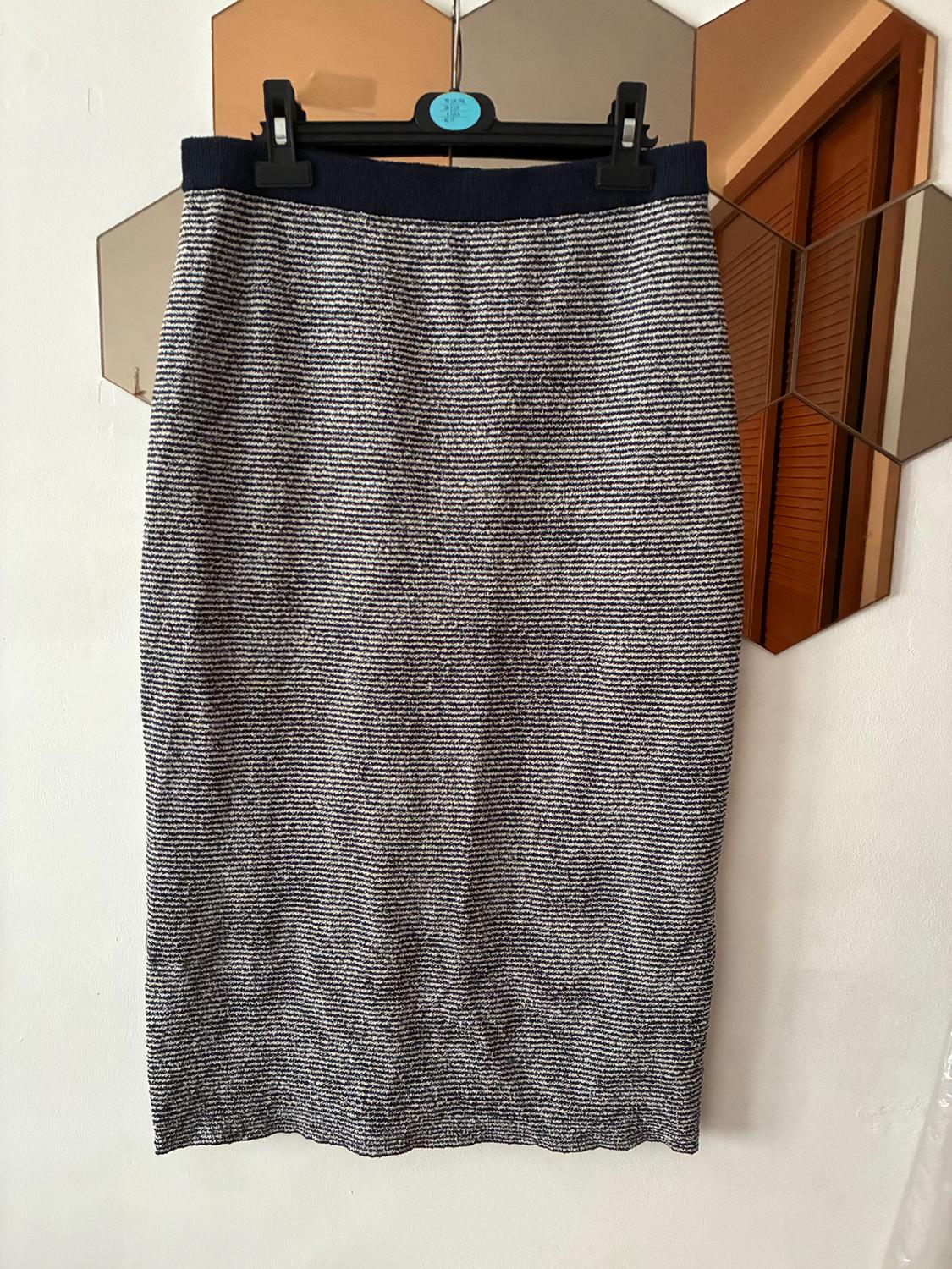 Long black and white striped skirt hanging on a black hanger, with a background of hexagonal mirrors and a white wall.