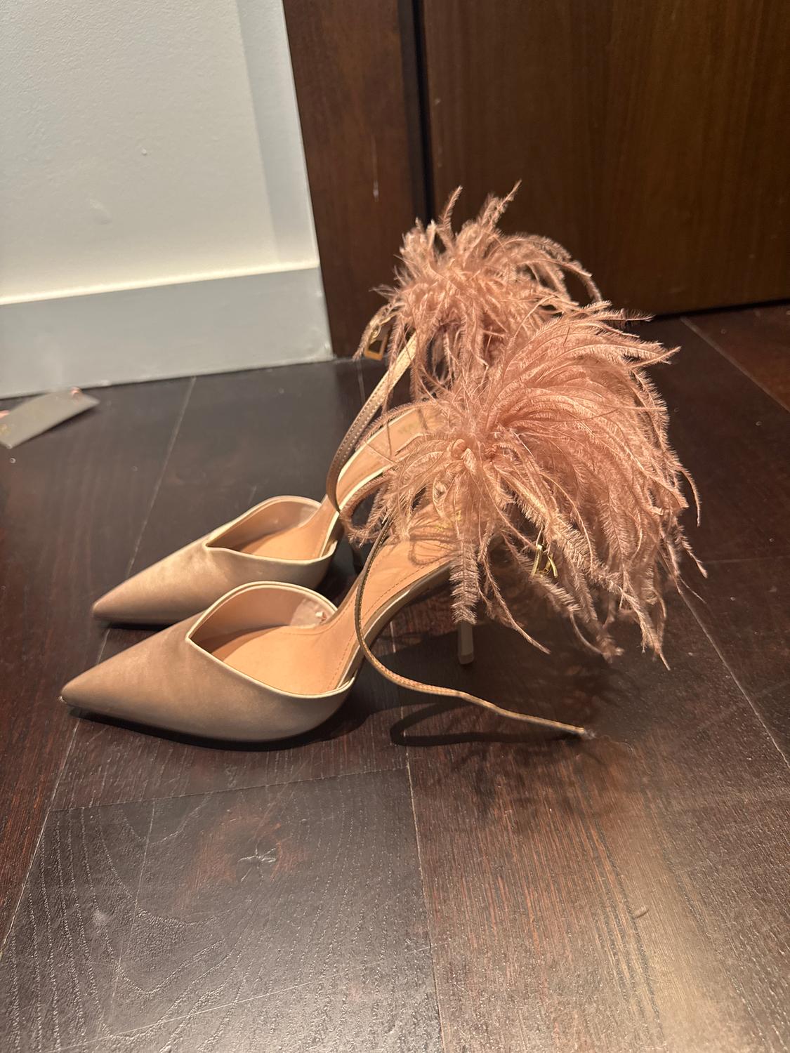 Beige high heels with decorative feathers on the heel, on a dark wooden floor.