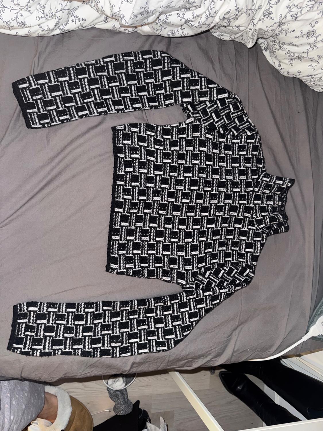 Black and white knitted jumper with a geometric pattern on a bed with white and grey sheets.