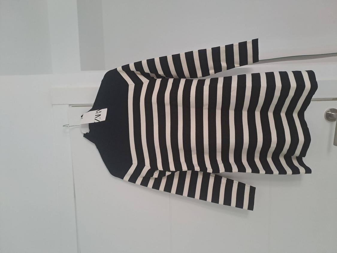 Black and white striped long-sleeved jumper with a black top, hanging on a white door. Label with the text ZARA.