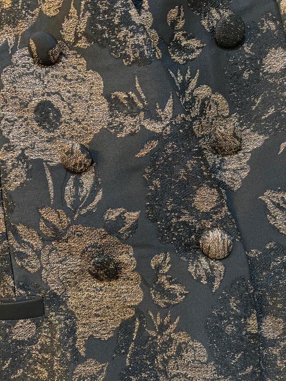 Black fabric with gold floral print and covered buttons. Elegant and detailed design in close-up.