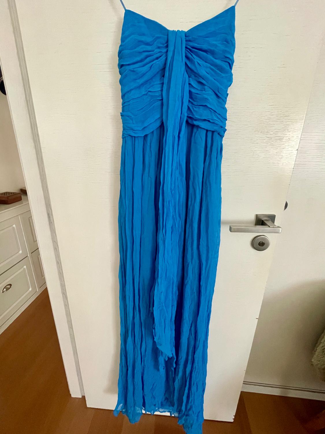 Long blue dress with a ruched bodice and front drape detail, hanging on a white interior door with a wooden floor.