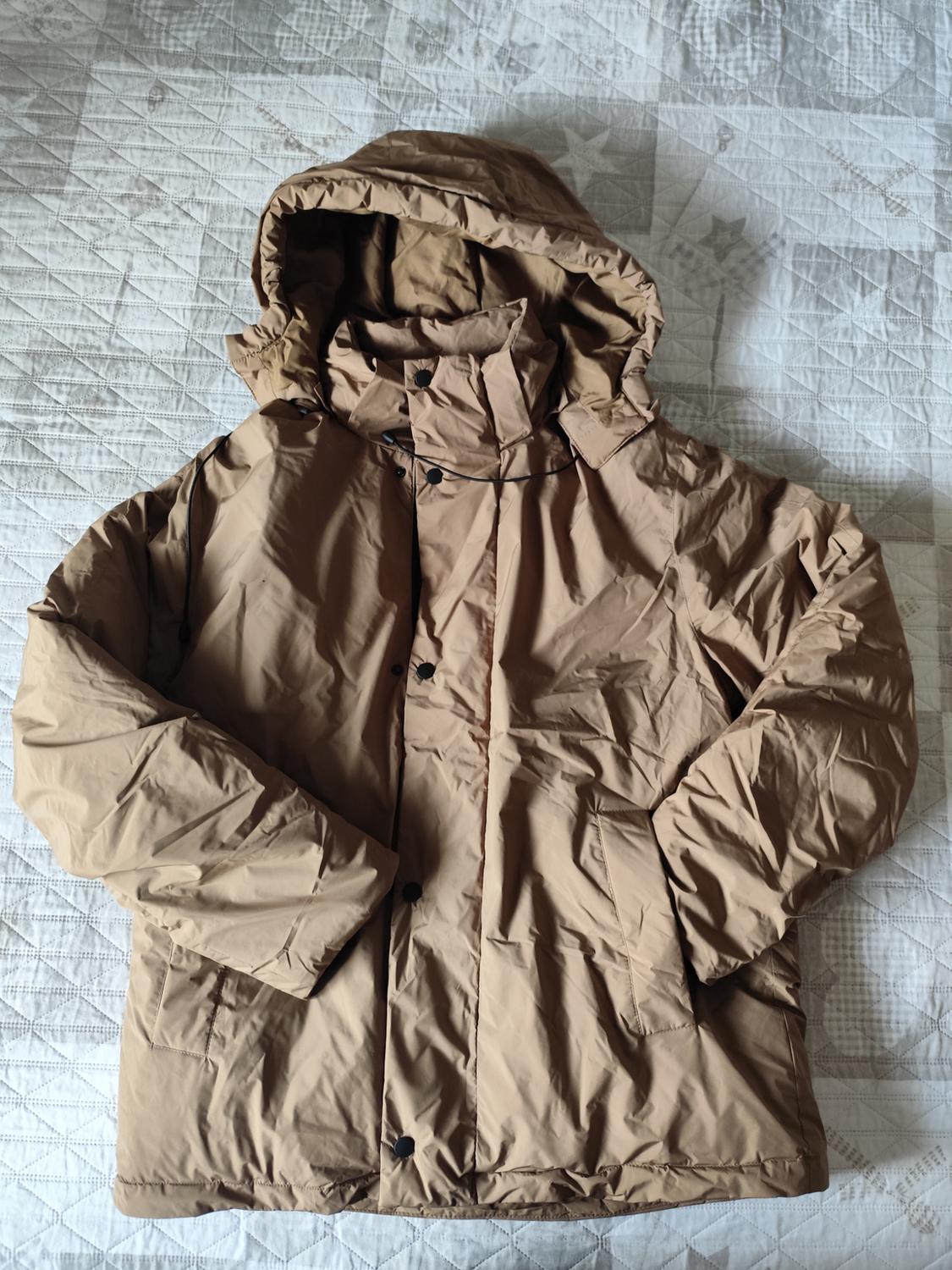 Light brown quilted jacket with a hood, black buttons, and pockets, on a white quilt with a diamond design.