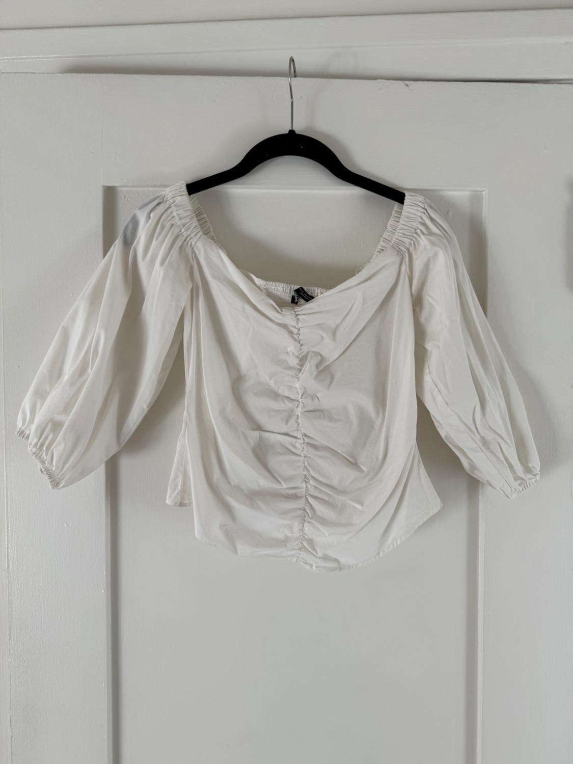 Front view of a white blouse with puffed sleeves and central gathering.