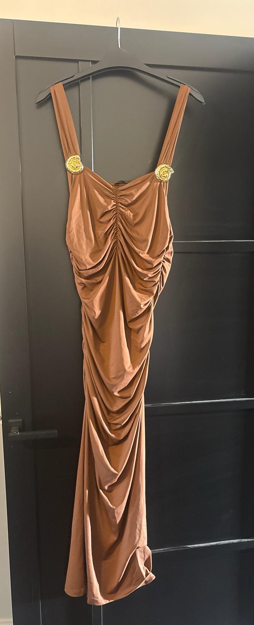 Brown dress with front ruching and gold details on the straps, hanging from a hanger on a black door.