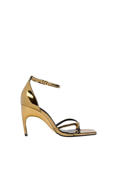 Gold, mid-heel sandal with thin straps and buckle fastening around the ankle, on a white background.