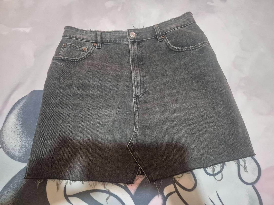 Grey denim skirt with frayed hem on a light-toned artistic background. Casual and modern design.
