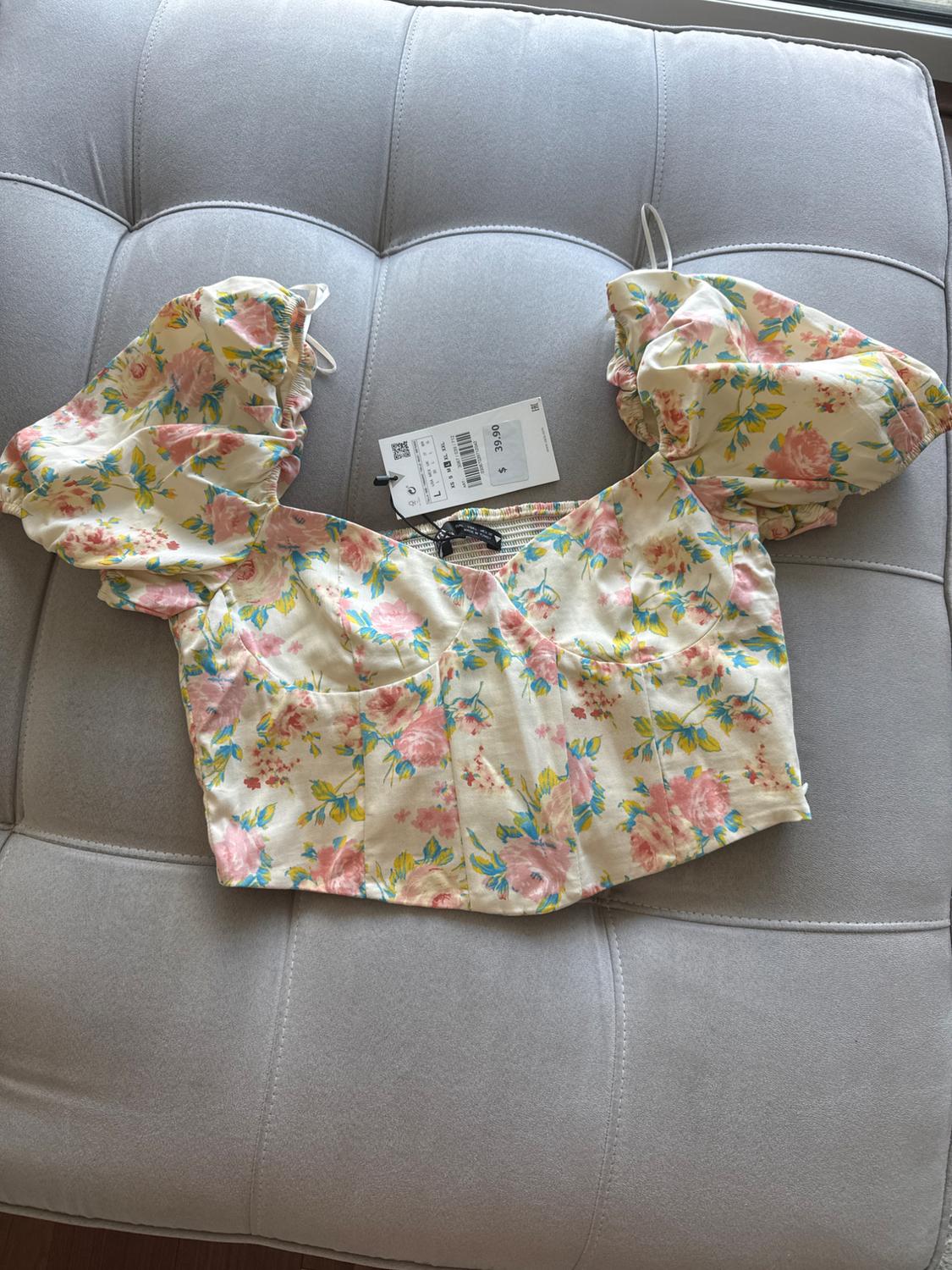Blouse courte à fleurs avec manches bouffantes sur un canapé gris. Étiquette visible avec un prix de 39,90 $.