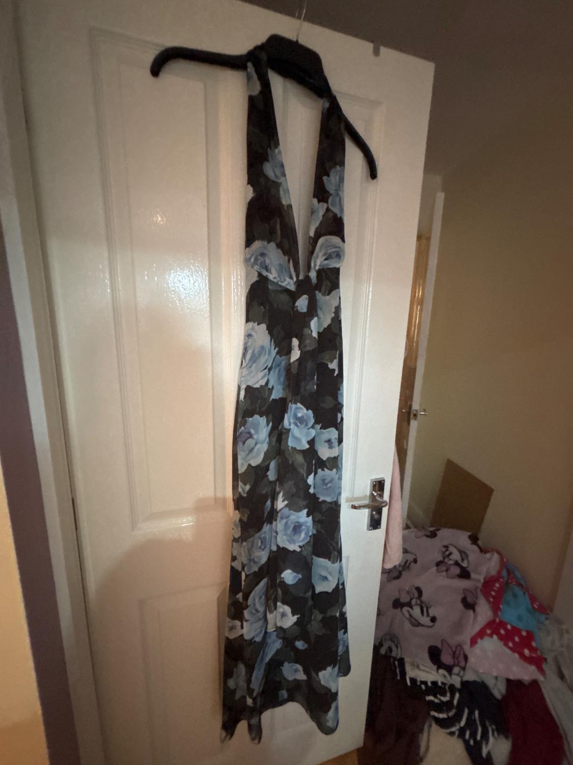 Dark-coloured maxi dress with a blue rose print and halter neck, hanging on a white door in a relaxed domestic setting.