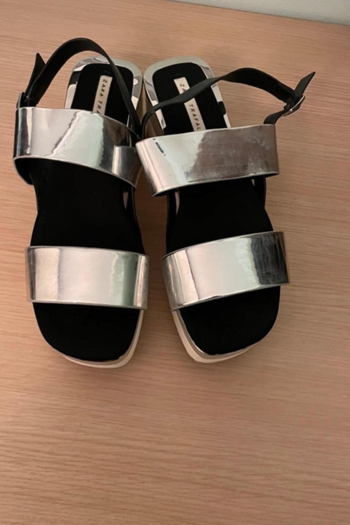Front view of black sandals with wide silver straps and side buckles.