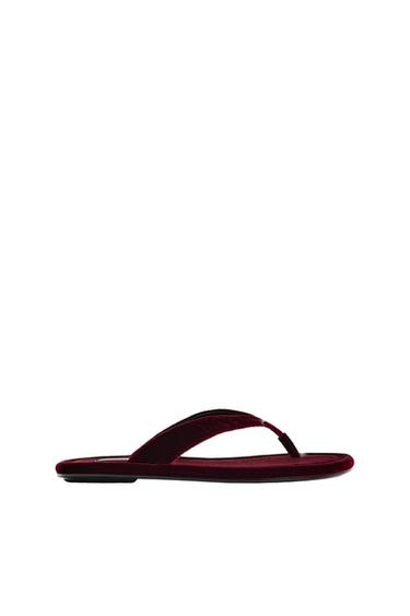 Burgundy velvet thong flat sandal seen from a side profile at the bottom. Minimalist composition with a wide white background.