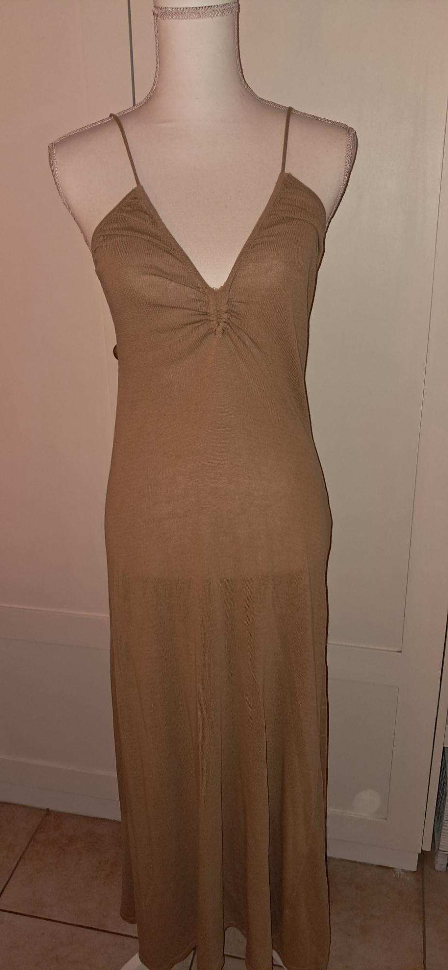 Mannequin wearing a long brown dress with thin straps and a ruched V-neck, in a relaxed indoor setting in front of white doors.