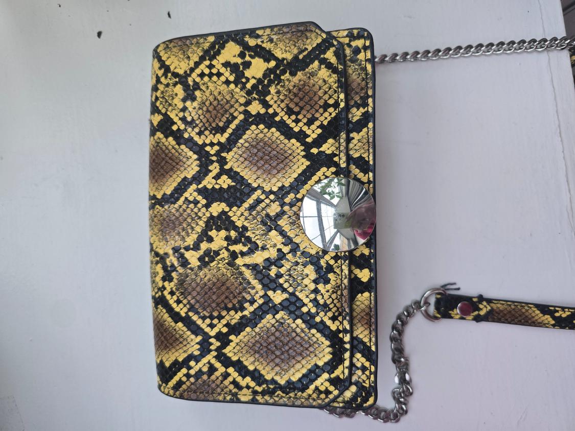 Detail of a yellow and black snake print handbag with a metal chain.
