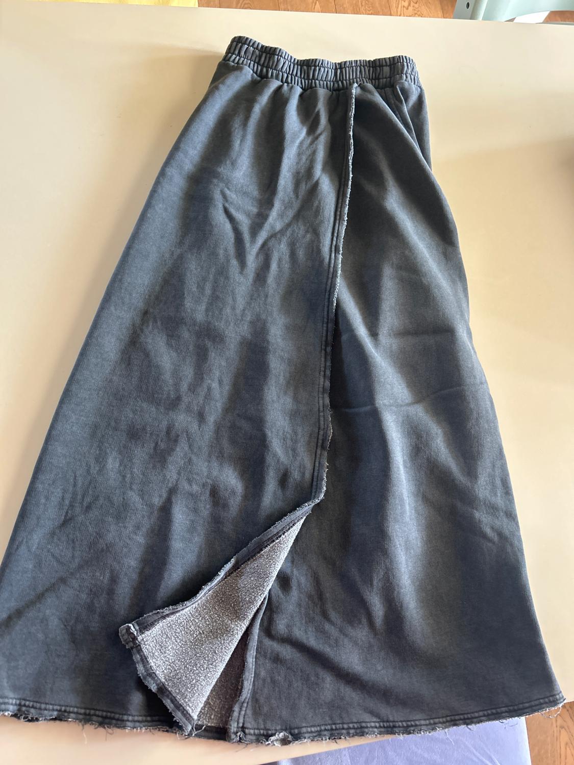Long grey skirt with elasticated waist and a slit at the hem, on a light surface. Visible inner fabric.