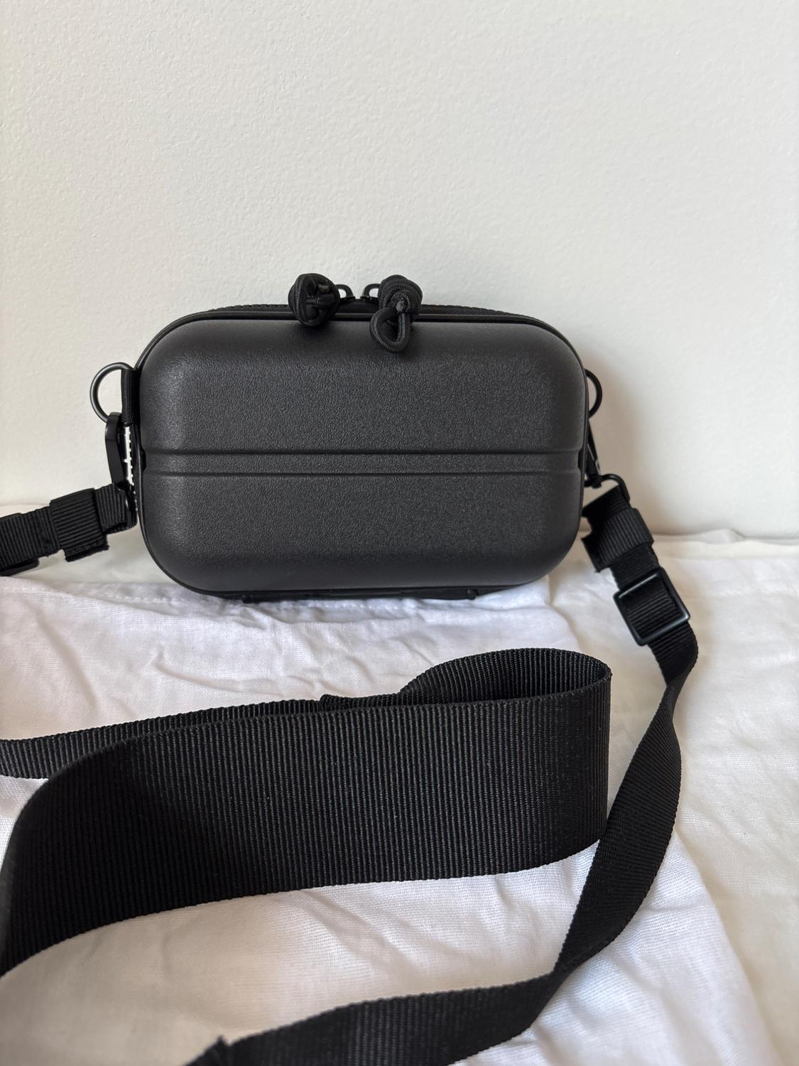 Rectangular black bag with adjustable strap on white fabric. Plain white background. Minimalist and modern design.