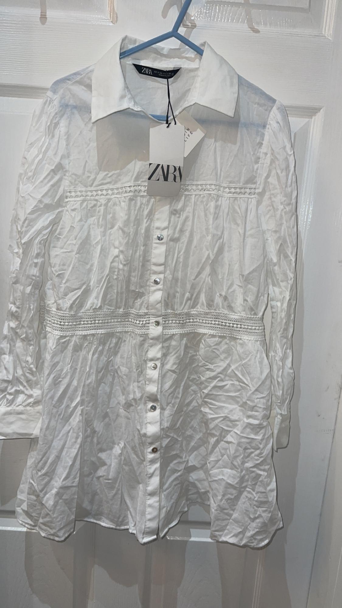 Front view of a white blouse with a classic collar, central button fastening, and horizontal lace detailing.
