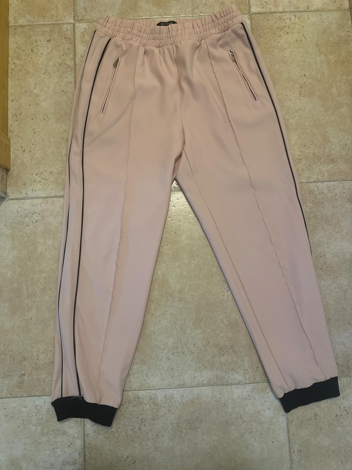 Light pink jogger trousers with an elasticated waist, zip pockets, and black detailing on the sides and ankles.