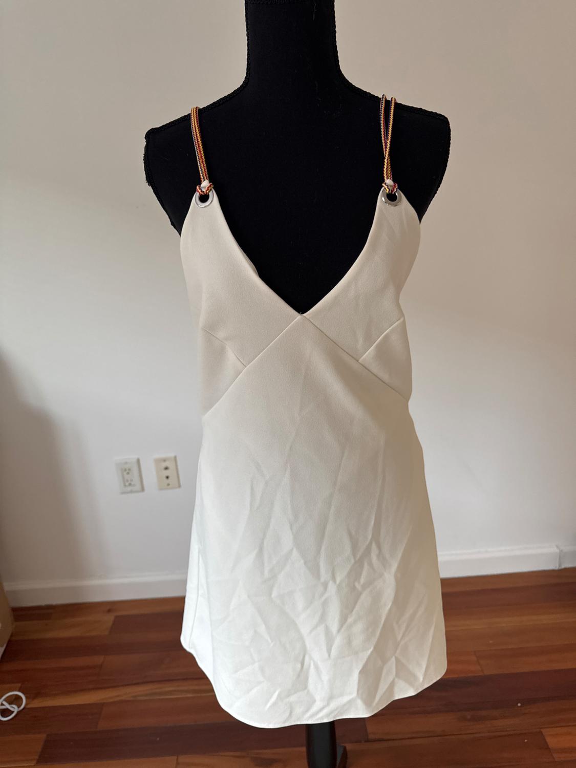 Front view of a white dress with thin straps and ring detail on the shoulders.