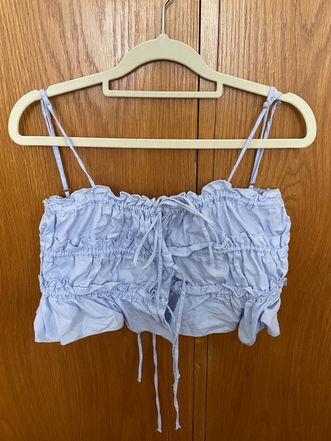 Light blue crop top with spaghetti straps and ruched detailing, hanging on a white coat hanger over a wooden door.