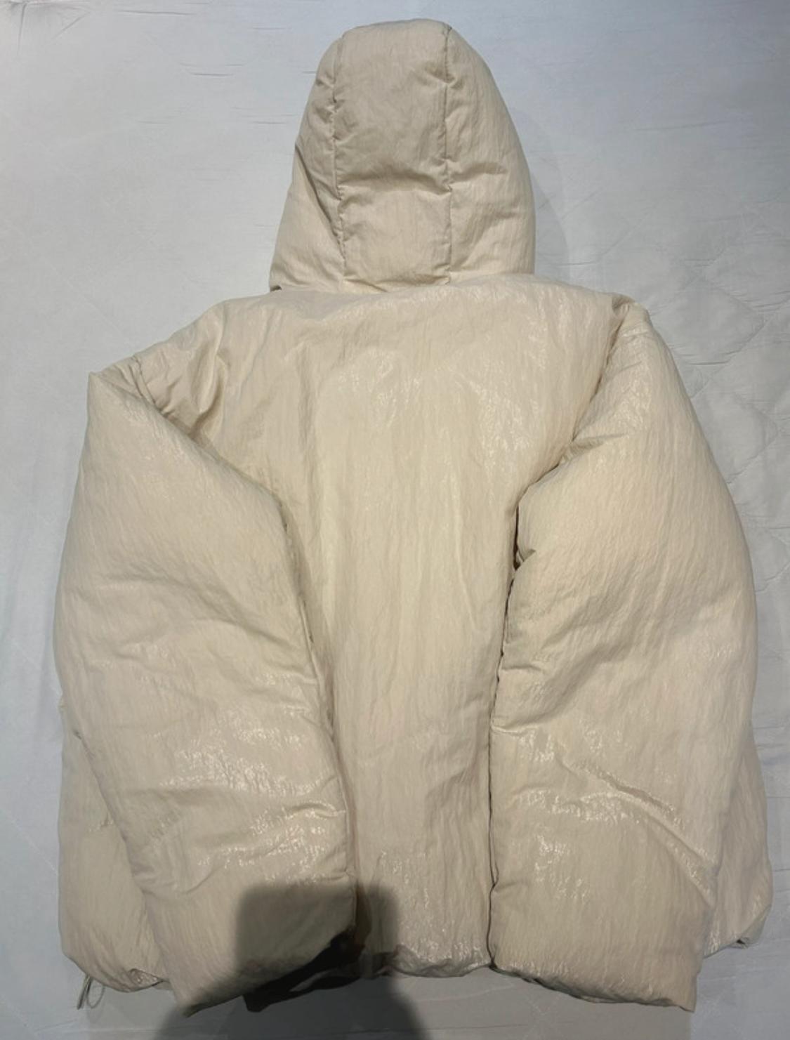 Beige padded jacket with hood, seen from behind on a light background. The texture is shiny and voluminous.