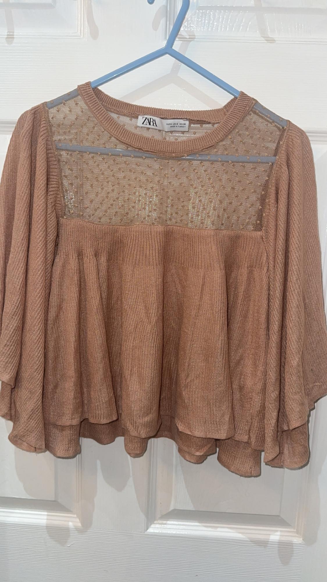 Front view of a brown blouse with a lace panel on the chest and wide sleeves.