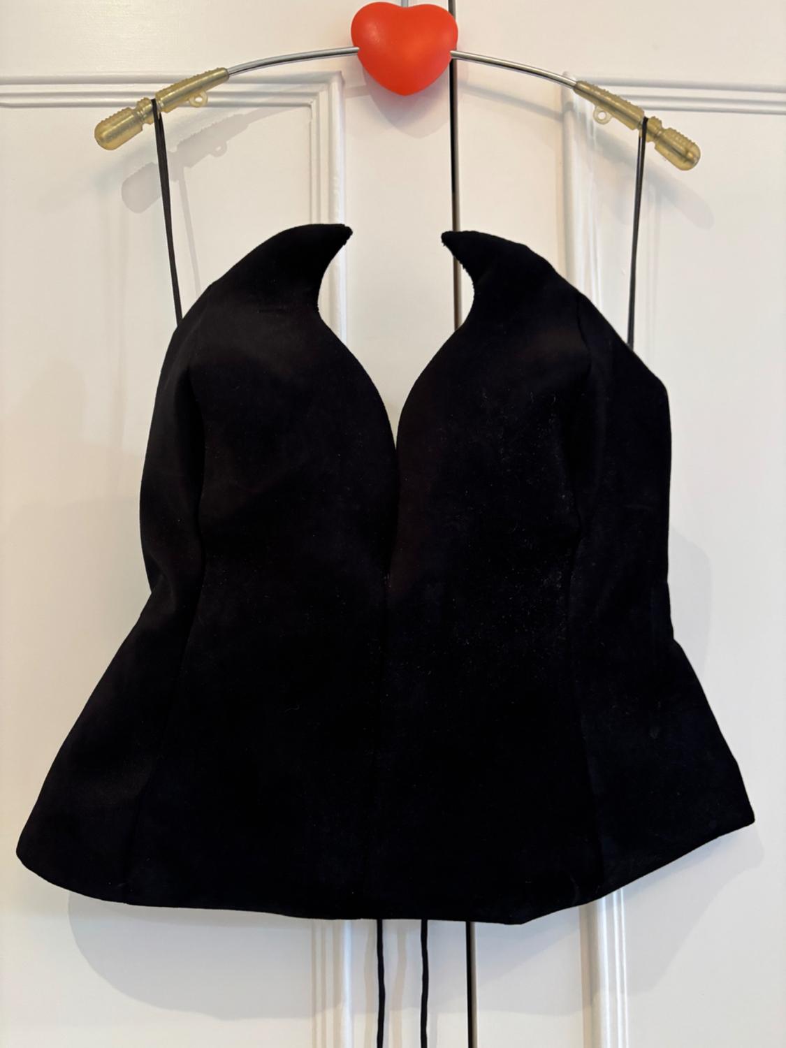Black camisole with spaghetti straps hanging on a red heart-shaped hanger, on a white door.