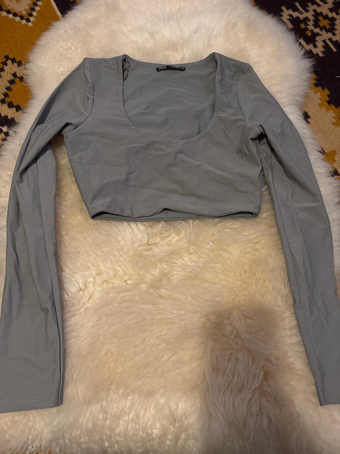 Grey long-sleeved top on a white fluffy rug, with a geometric pattern rug in brown and yellow tones in the background.