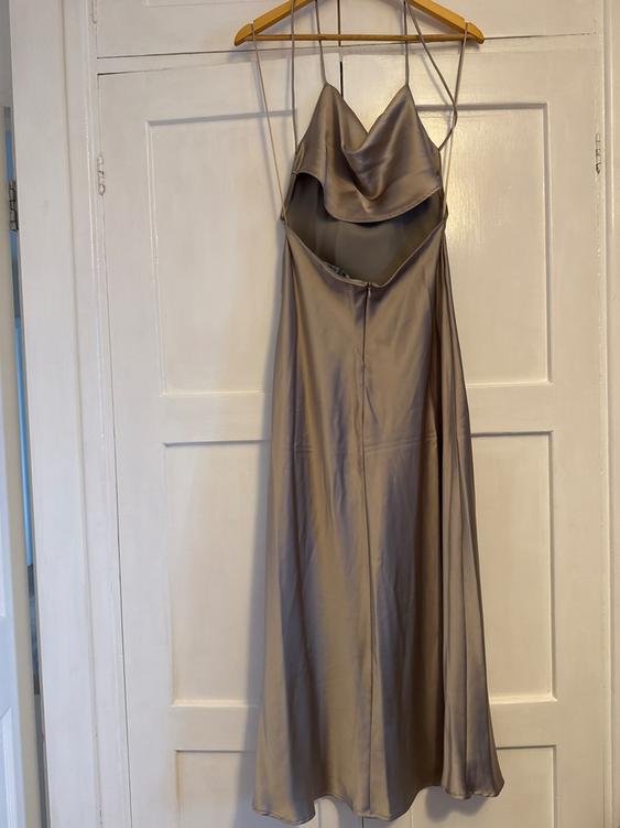 Beige satin dress hanging on a wooden hanger over a white door. Design with thin straps and a draped neckline.